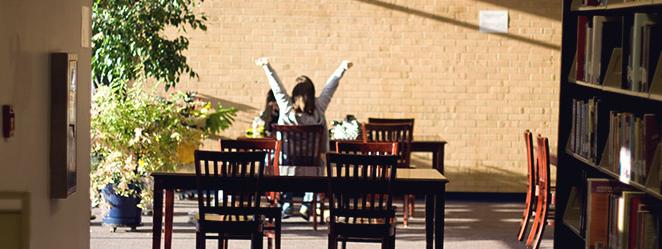 Student stretching at tables in library